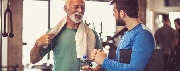 Ein junger Fitnesstrainer spricht mit einem älteren Kunden im Studio