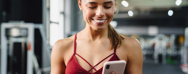 Attraktive junge Frau im Fitnessstudio mit Blick auf ihr Handy