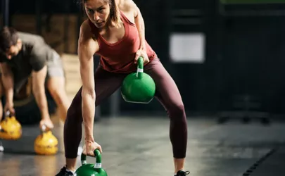 Weibliche Athletin beim Krafttraining mit Kettlebells im Fitnessstudio.