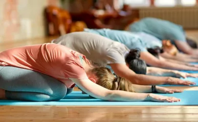 Fünf Menschen machen nebeneinander die Übung Kindhaltung beim Yoga