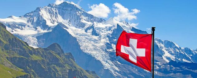 Eine Schweizer Fahne weht im Vordergrund, dahinter sind die Schweizer Berge zu sehen